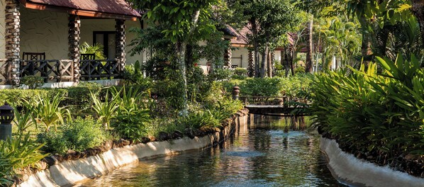 Un jardín tranquilo con un estrecho canal de agua, muros de piedra y abundante vegetación.