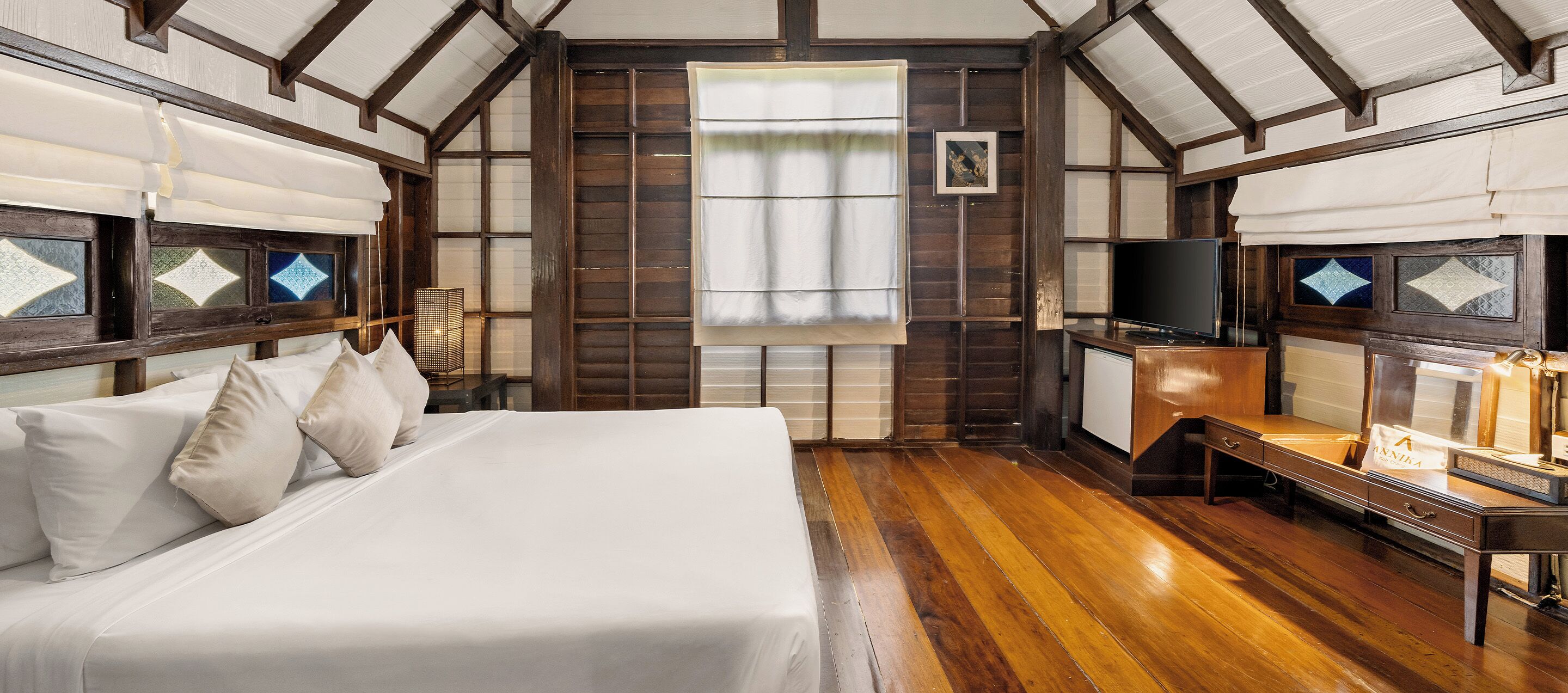 A traditional Japanese-style room with tatami flooring, a large bed with white bedding, a television, and a small table with a lamp.