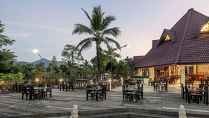 Een restaurant met terras, een betegeld dak en palmbomen.