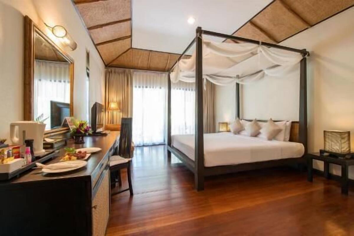 A four-poster bed with a canopy, a desk with a chair, a television, and a window with curtains.