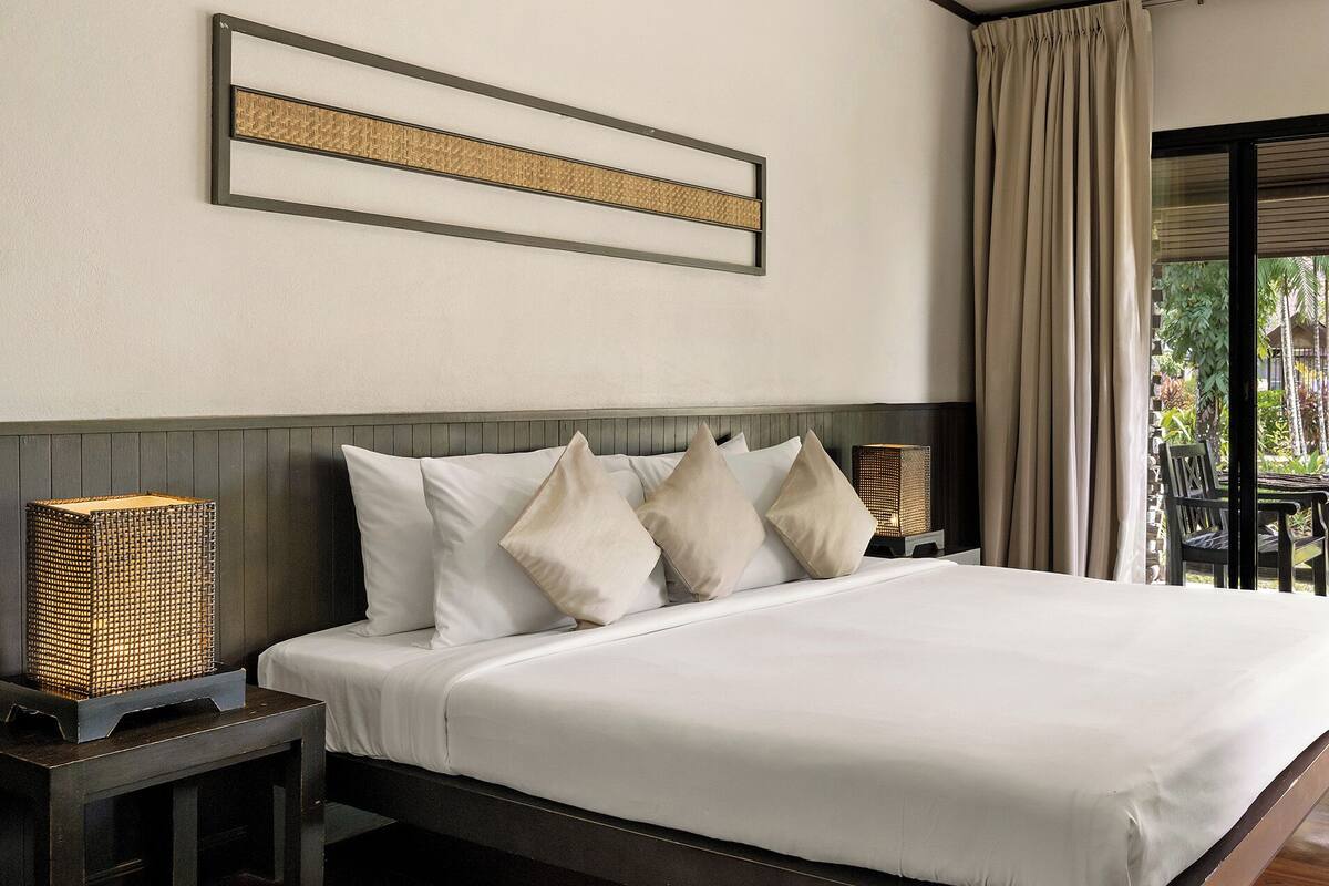 A hotel room with a bed, a nightstand, a lamp, a chair, and a view of the outdoors.