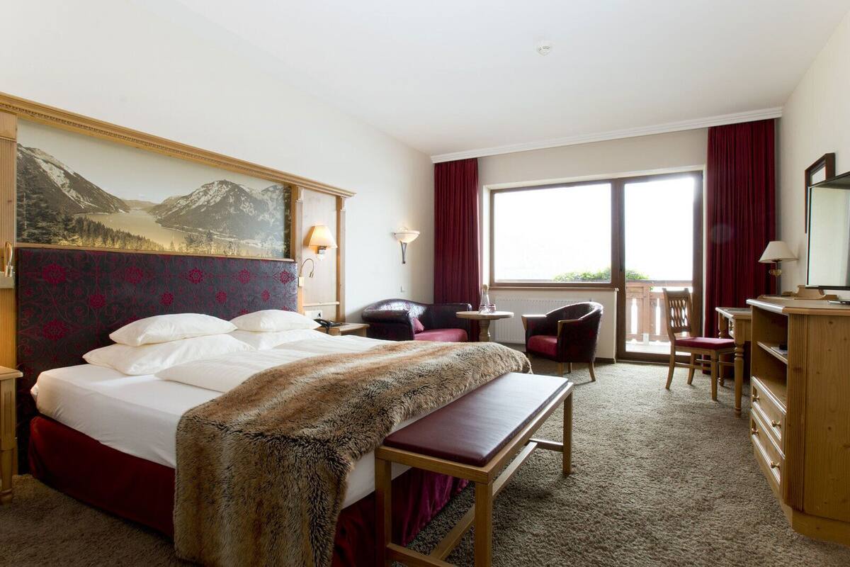Ein Hotelzimmer mit einem großen Bett, einem Schreibtisch, einem Sessel, einem kleinen Tisch und Blick ins Freie.