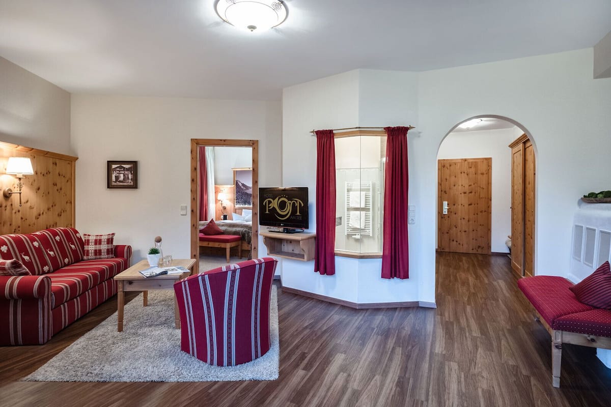 Ein Hotelzimmer mit Holzboden, einem roten Sofa, einem gestreiften Sessel, einem Fernseher und einem Holzschrank.