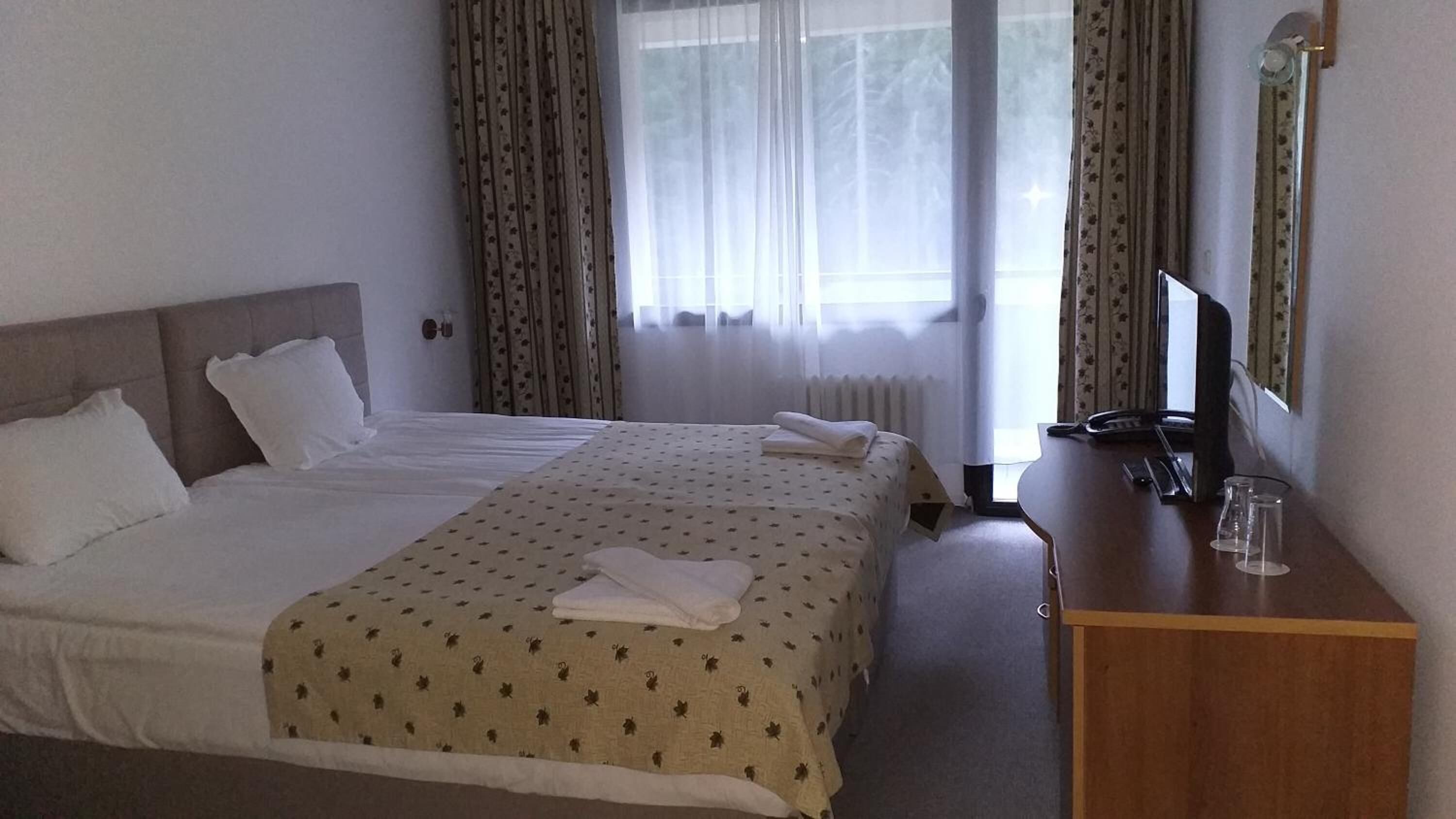 Una habitación de hotel con una cama grande, un escritorio de madera, un televisor y una ventana con cortinas.