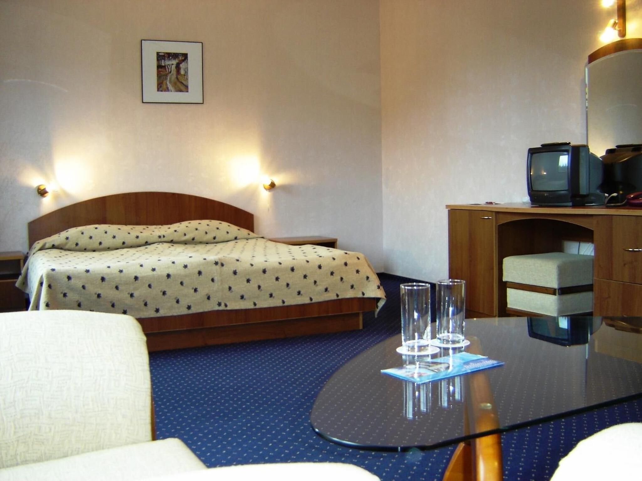 Habitació d'hotel amb un llit, un escriptori amb un ordinador i una televisió, i una taula petita amb gots i un menú.