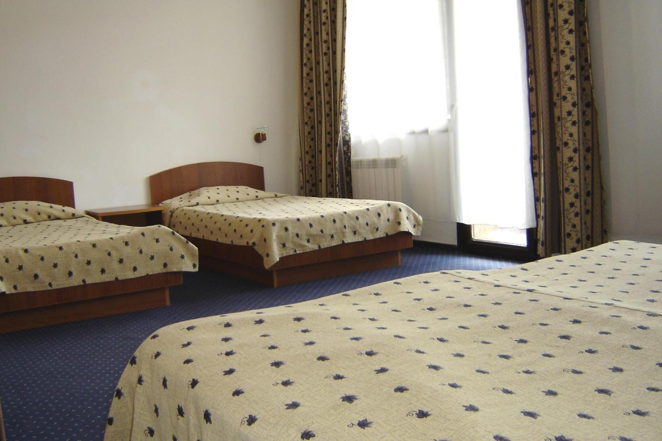 A hotel room with two single beds, a wooden headboard, a nightstand, and a window with curtains.