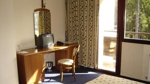 Una habitación con escritorio de madera, una silla, televisor y ventana con cortinas.