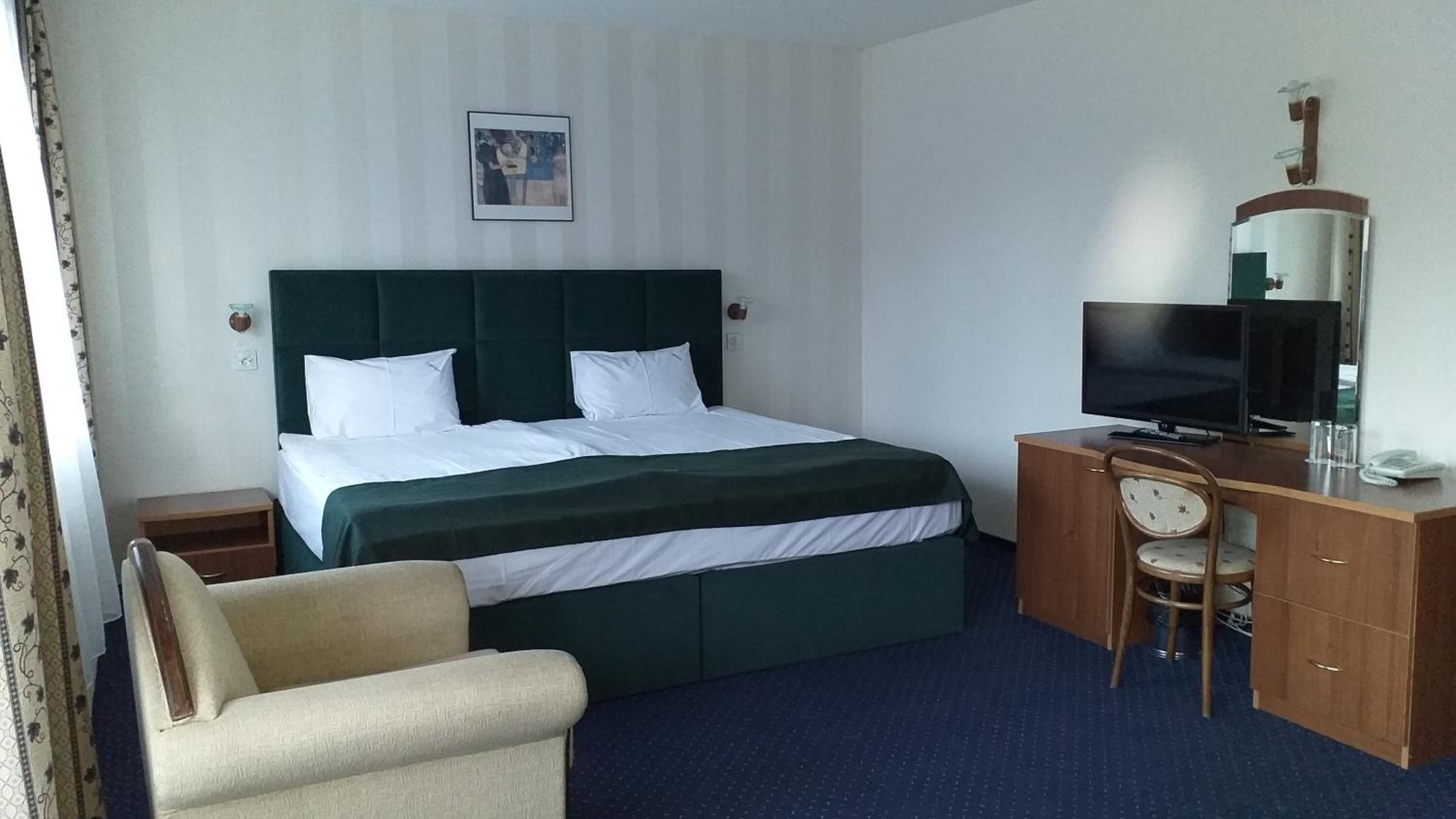 A hotel room with a bed, a desk with a TV, a chair, and a small table.