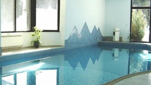 Una piscina interior con agua azul cristalina, suelo de baldosas y una pared decorativa con un motivo de montaña.