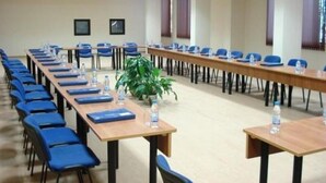 Un salón de conferencias con mesas largas y sillas azules, equipado con botellas de agua y carpetas.