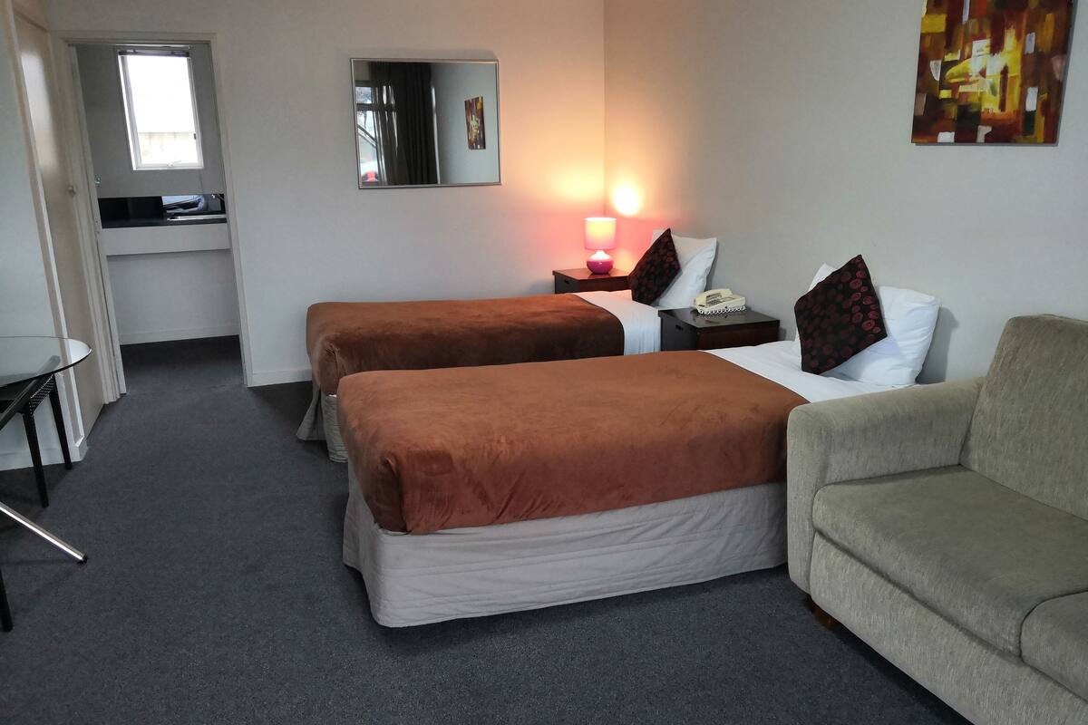 Habitación de hotel con dos camas, un sofá, un escritorio y una lámpara.