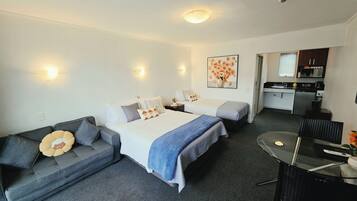 Habitación de hotel con dos camas, un sofá, una mesa de comedor y una kitchenette.