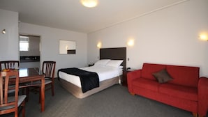Een hotelkamer met een bed, een rode bank, een eettafel met stoelen en een kleine kitchenette.