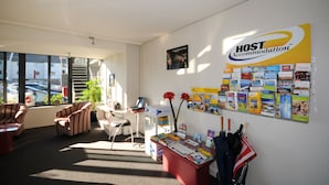A reception area with a desk, chairs, a computer, a wall with a 'HOST Accommodation' sign, and various informational brochures. - City Central Motel Apartments (Christchurch)