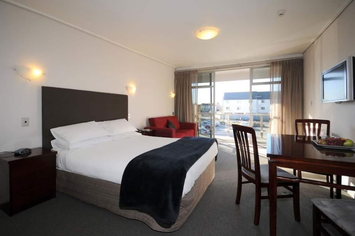 Habitación de hotel con una cama, un escritorio, una silla, un televisor y una ventana con vistas a edificios.