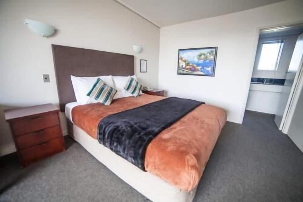 Una habitación de hotel con una cama, un tocador, un cuadro en la pared y una ventana.