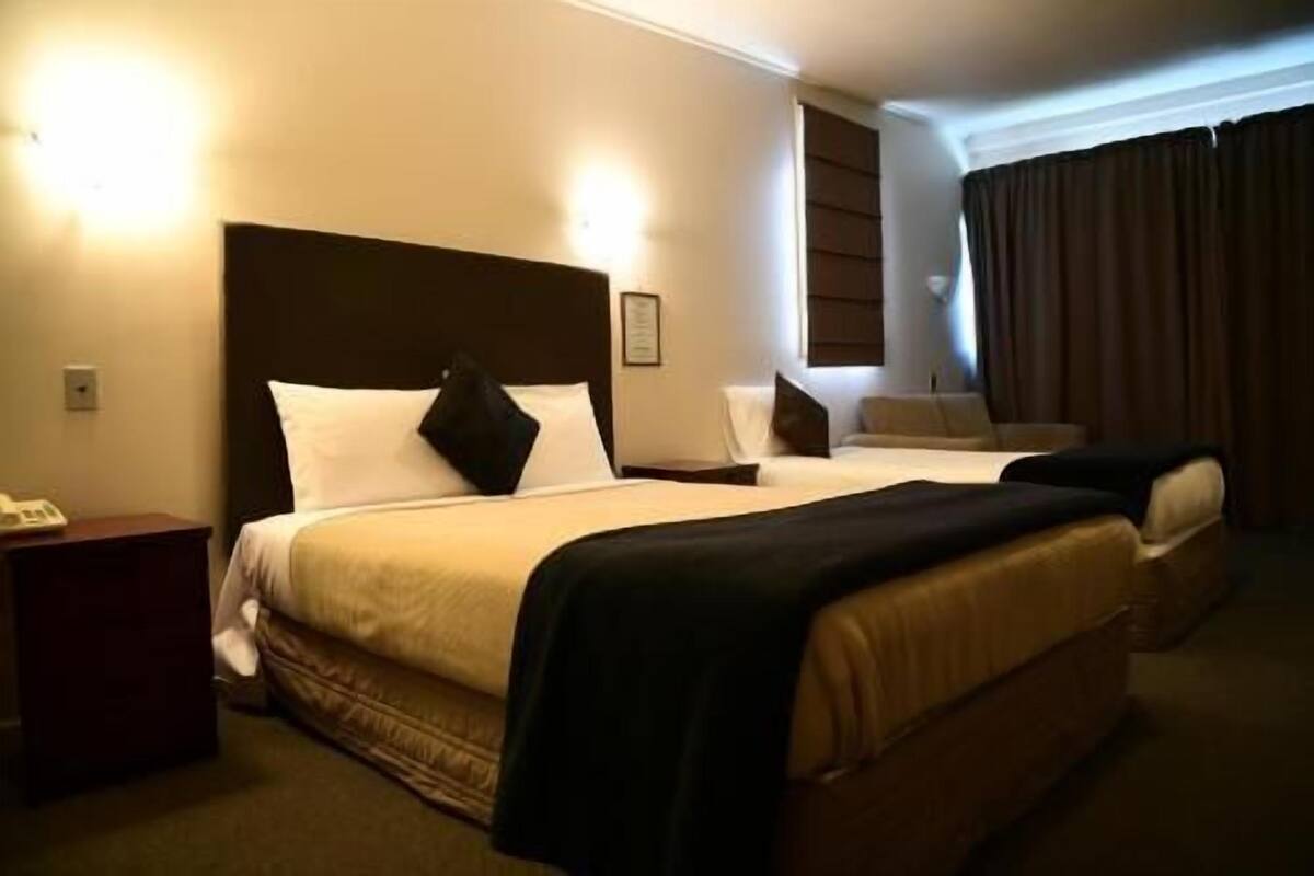 Una habitación de hotel con dos camas, una mesita de noche, una lámpara y una ventana con cortinas.