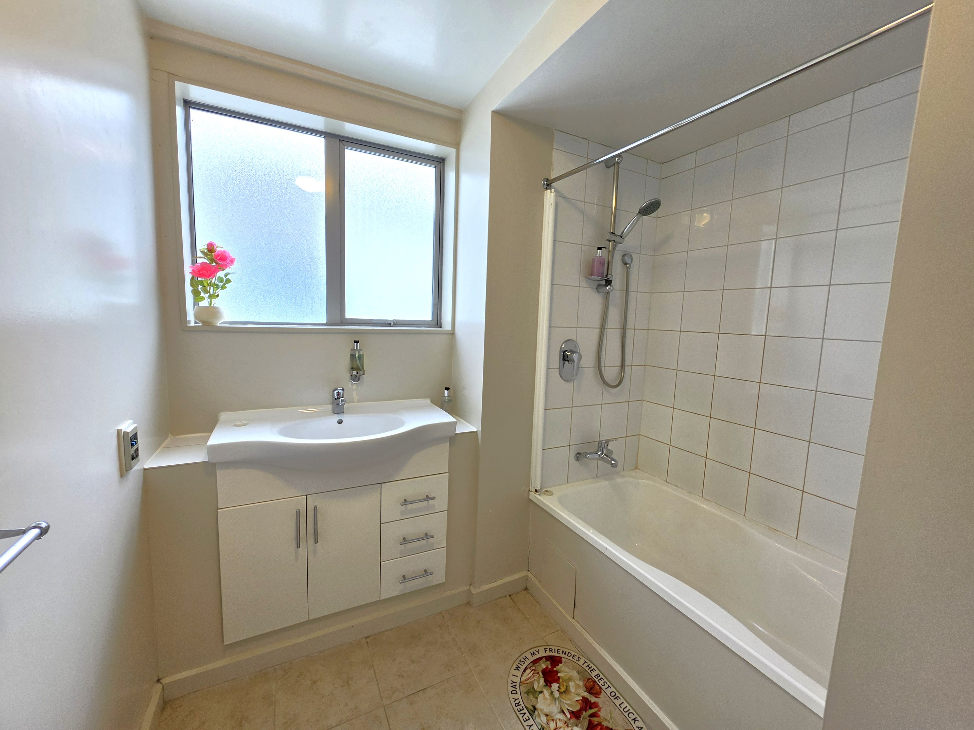 Un bagno con un lavandino bianco, una finestra sopra e uno spazio doccia con porta in vetro.