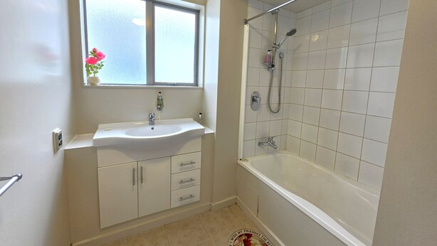 Ein Badezimmer mit einem weißen Waschbecken, einem Fenster darüber und einer Duschkabine mit Glastür.