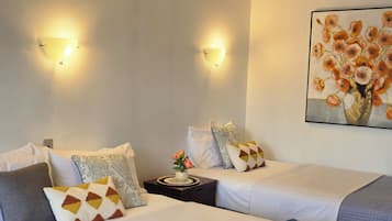 A hotel room with two beds, a nightstand, a vase with flowers, and a painting on the wall.