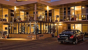 Een hotel met een glazen gevel, meerdere verdiepingen en een auto ervoor geparkeerd.