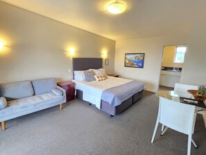Une chambre d’hôtel avec un lit, un canapé, une petite table et une chaise. Il y a un tableau au mur et une fenêtre.