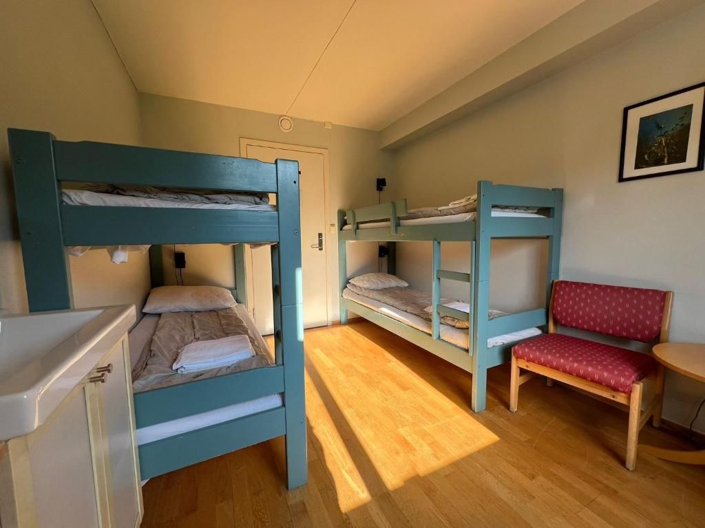 A dormitory room with bunk beds, a desk, a chair, and a small table.