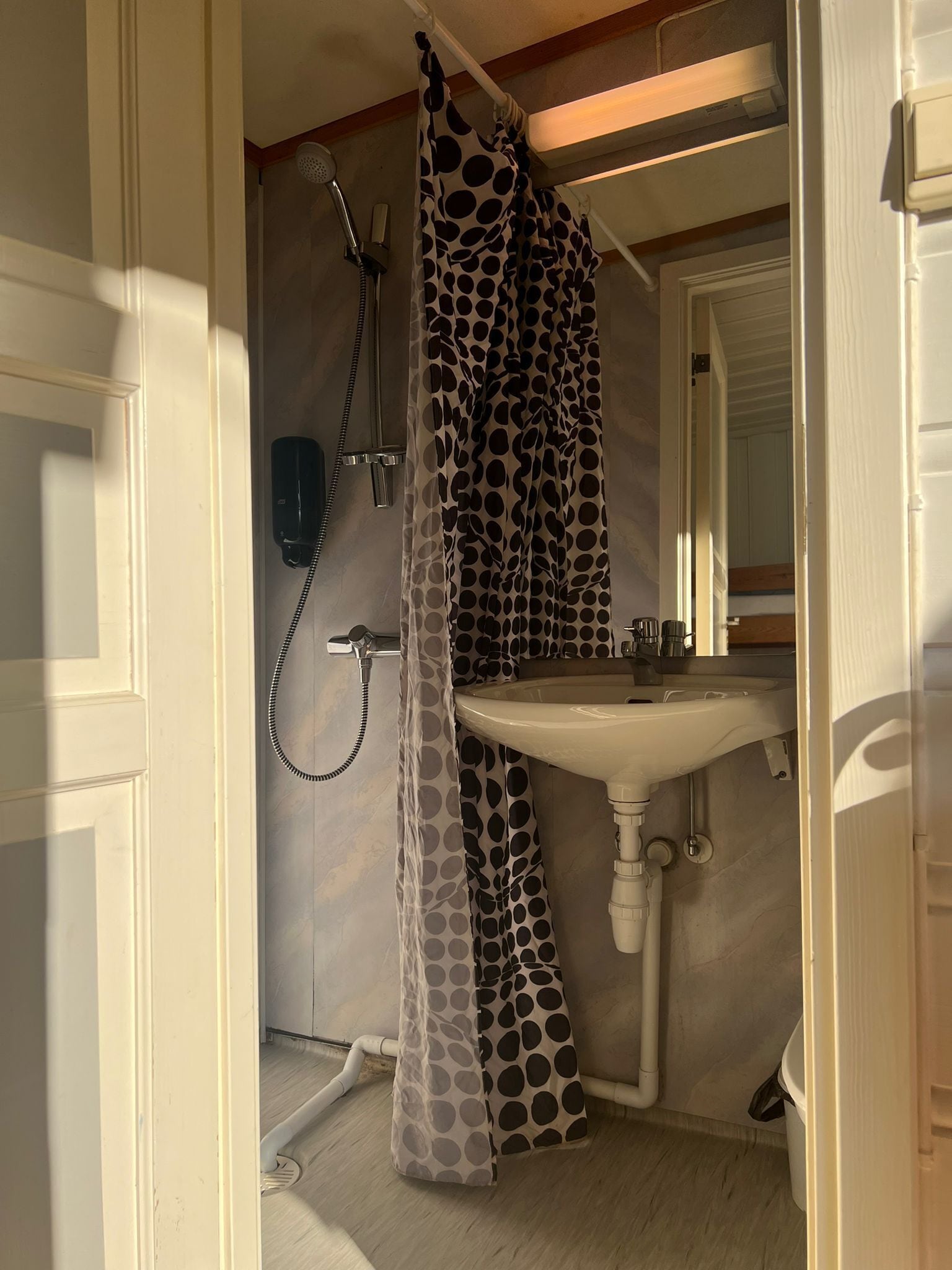 A bathroom with a white sink, a shower with a polka dot shower curtain, and a telephone mounted on the wall.