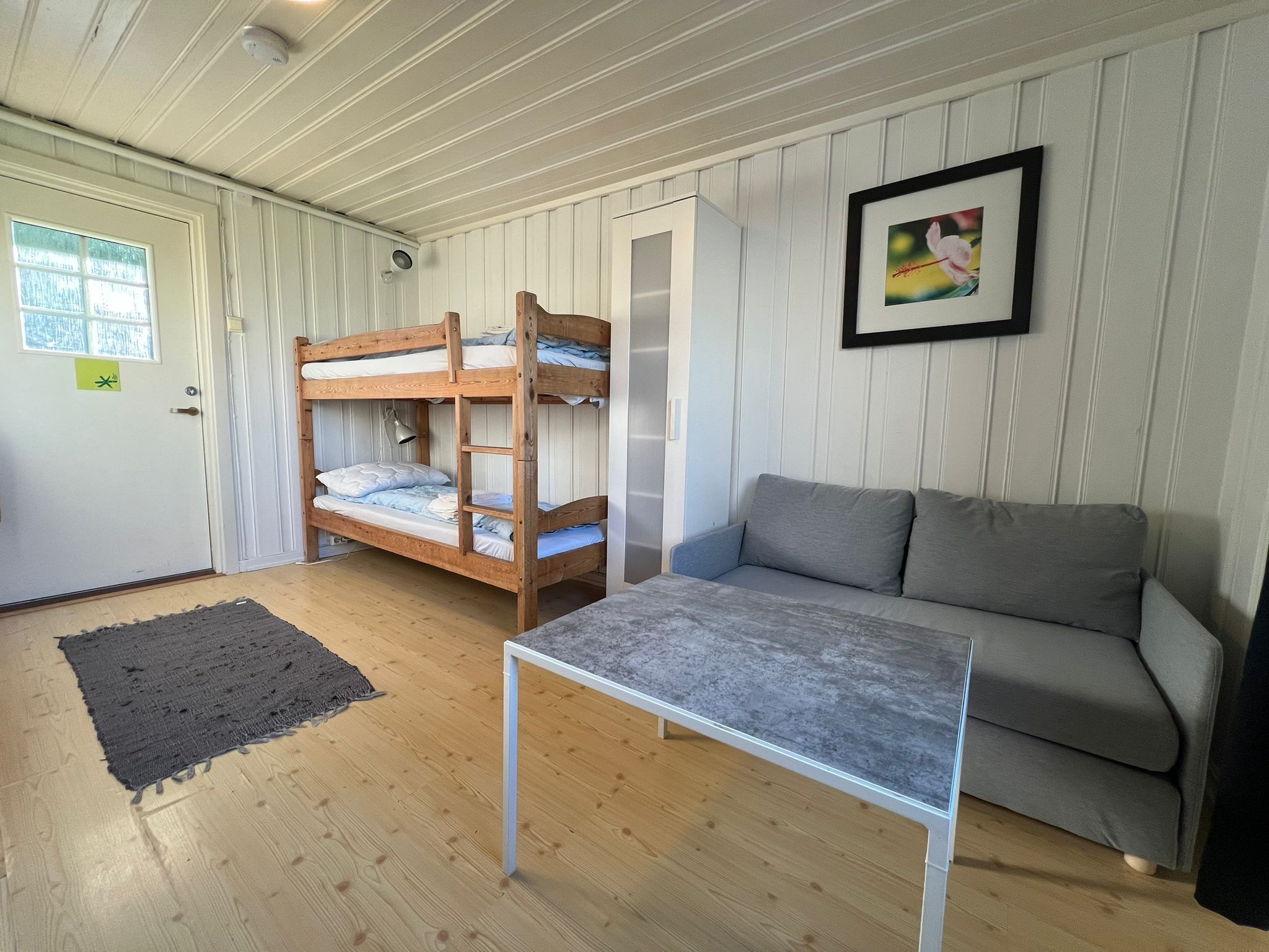 A room with bunk beds, a grey sofa, a small table, and a framed picture on the wall.