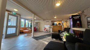 A spacious lobby with a wooden ceiling, a reception desk, seating areas, and a vending machine. - Hovdetun - Gjøvik Vandrerhjem - Hostel (Gjovik)