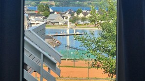 A view of a swimming pool area with a wooden deck, a tennis court, and a body of water. - Hovdetun - Gjøvik Vandrerhjem - Hostel (Gjovik)