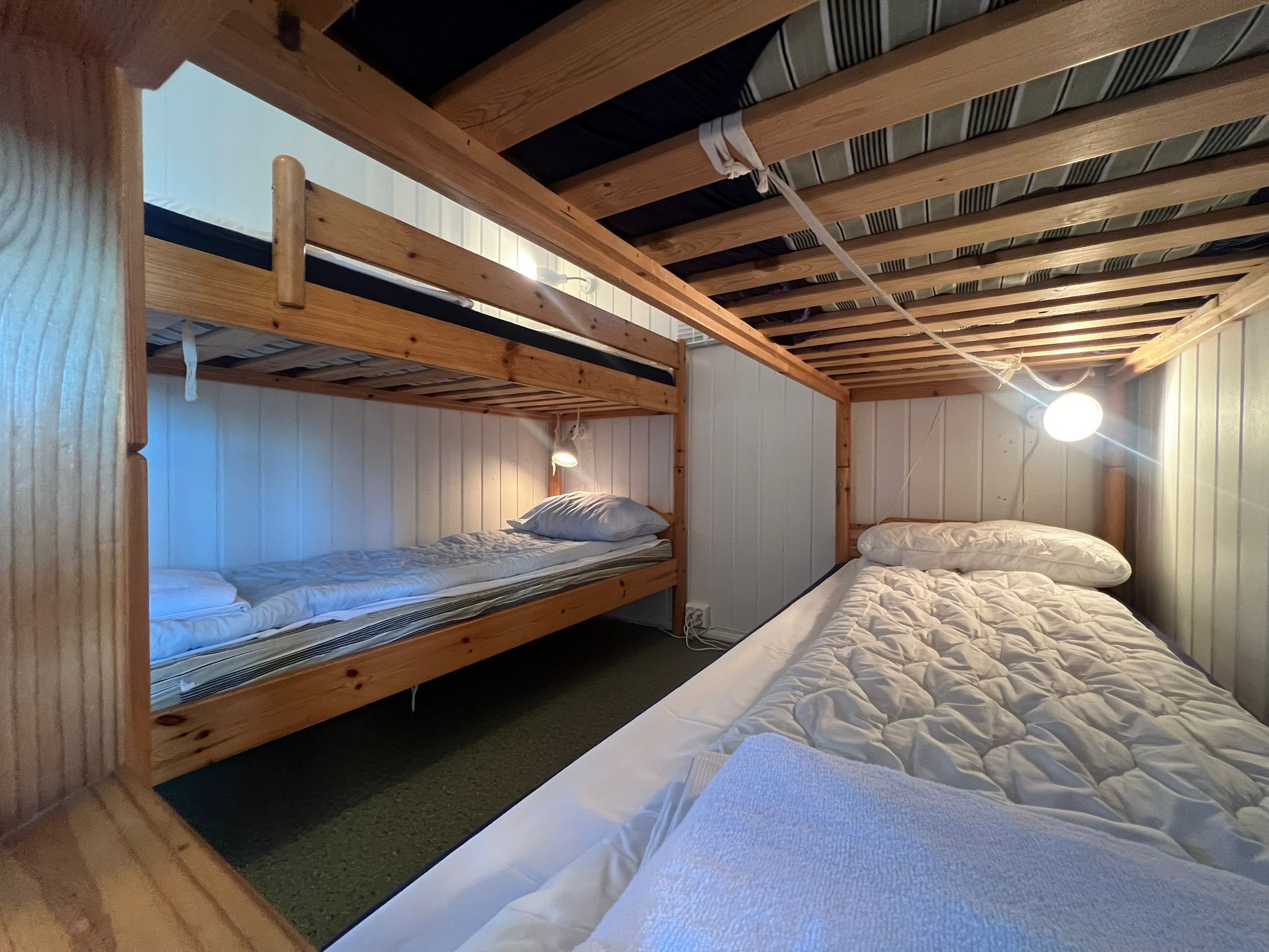 A bunk bed room with wooden beams, a single bed, and a nightstand.