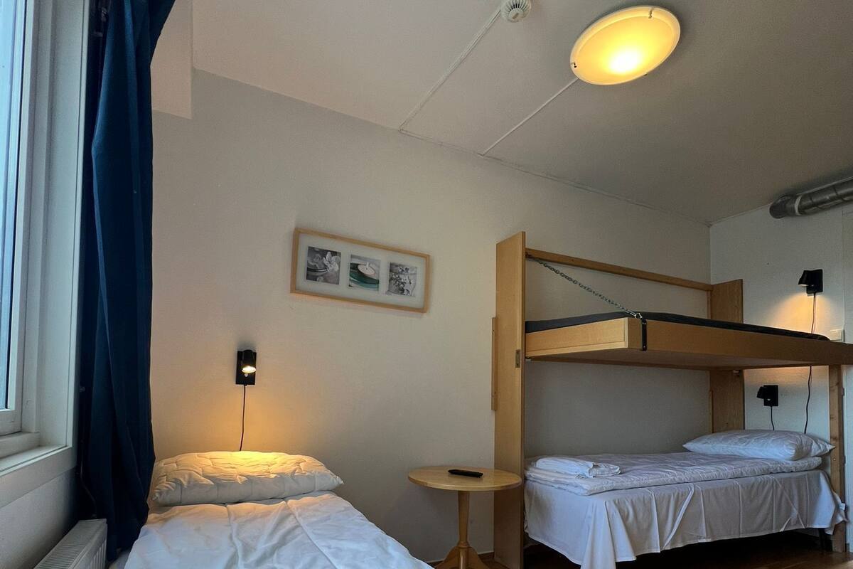 Ein Zimmer mit zwei Betten, einem kleinen Tisch, einem Wandbild und einem Fenster mit Vorhängen.