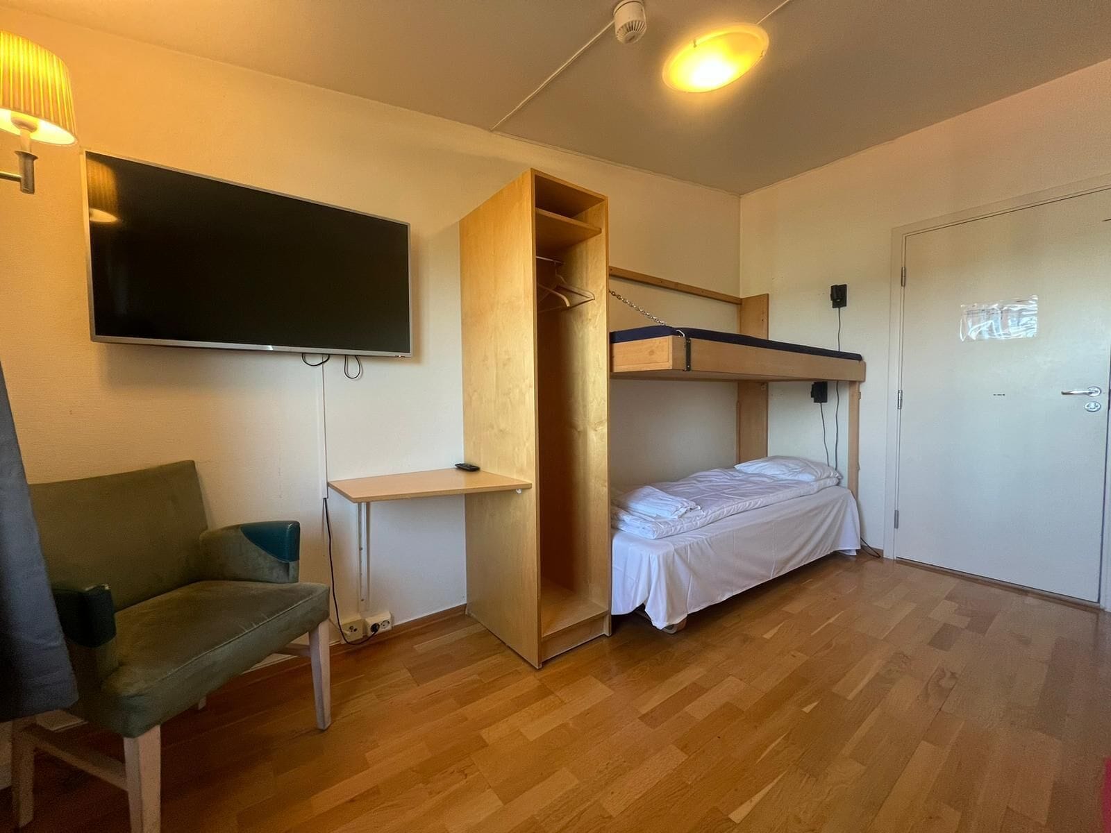 Een kleine kamer met een stapelbed, een bureau, een stoel en een aan de muur bevestigde televisie.
