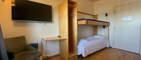 Habitación compacta con literas, un escritorio, una silla y un televisor montado en la pared.