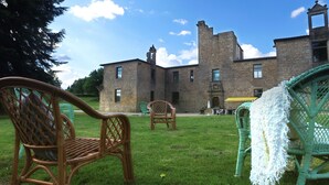 Un bâtiment en pierre avec une grande pelouse et des chaises en osier.