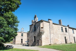 Un bâtiment en pierre doté d’un clocher, une cour avec une table de pique-nique et une zone herbeuse.