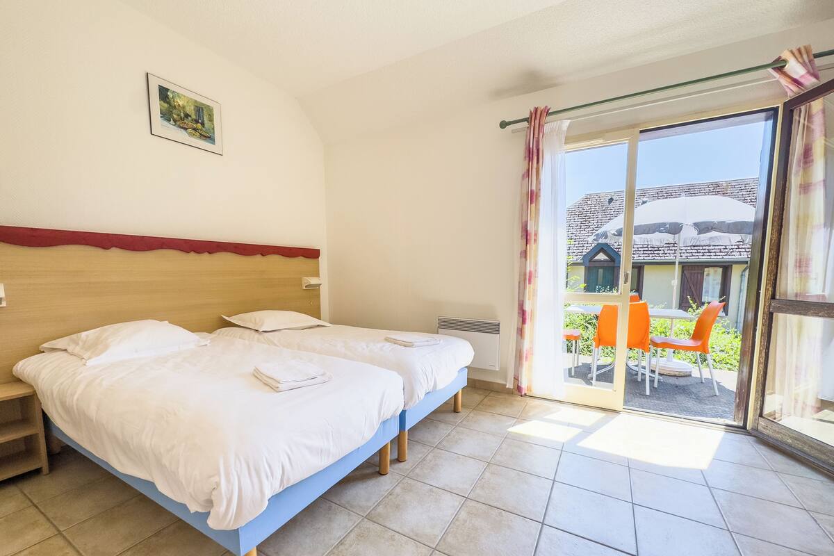 Une chambre d’hôtel avec deux lits, une grande fenêtre donnant sur l’extérieur et une petite table avec des chaises.