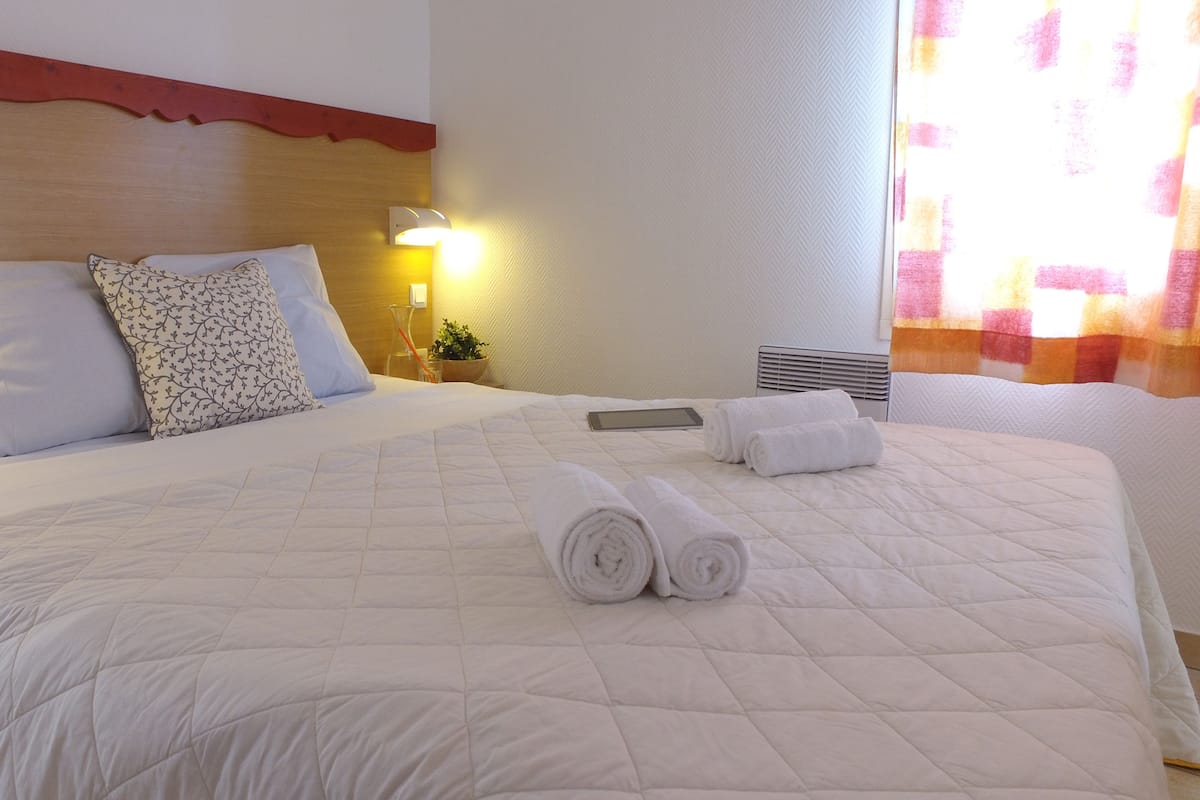 Une chambre d’hôtel avec un grand lit, deux oreillers, une table de chevet avec une lampe et une fenêtre avec des rideaux.