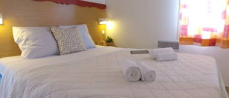 Una camera d'albergo con un letto grande, due cuscini, un comodino con una lampada e una finestra con tende.
