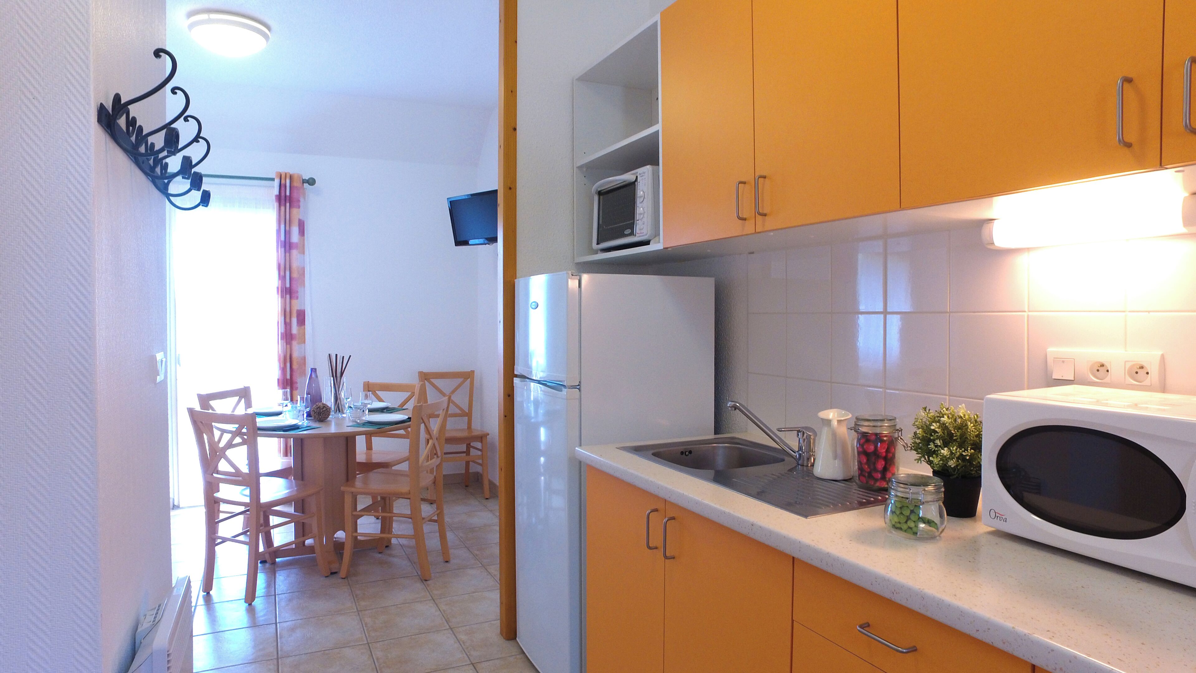 Une cuisine compacte comprenant une table à manger, des chaises, un réfrigérateur, un four à micro-ondes et un évier.