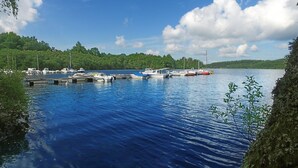 Un lac paisible où des bateaux sont amarrés à un quai, entouré d’une végétation luxuriante et sous un ciel dégagé.