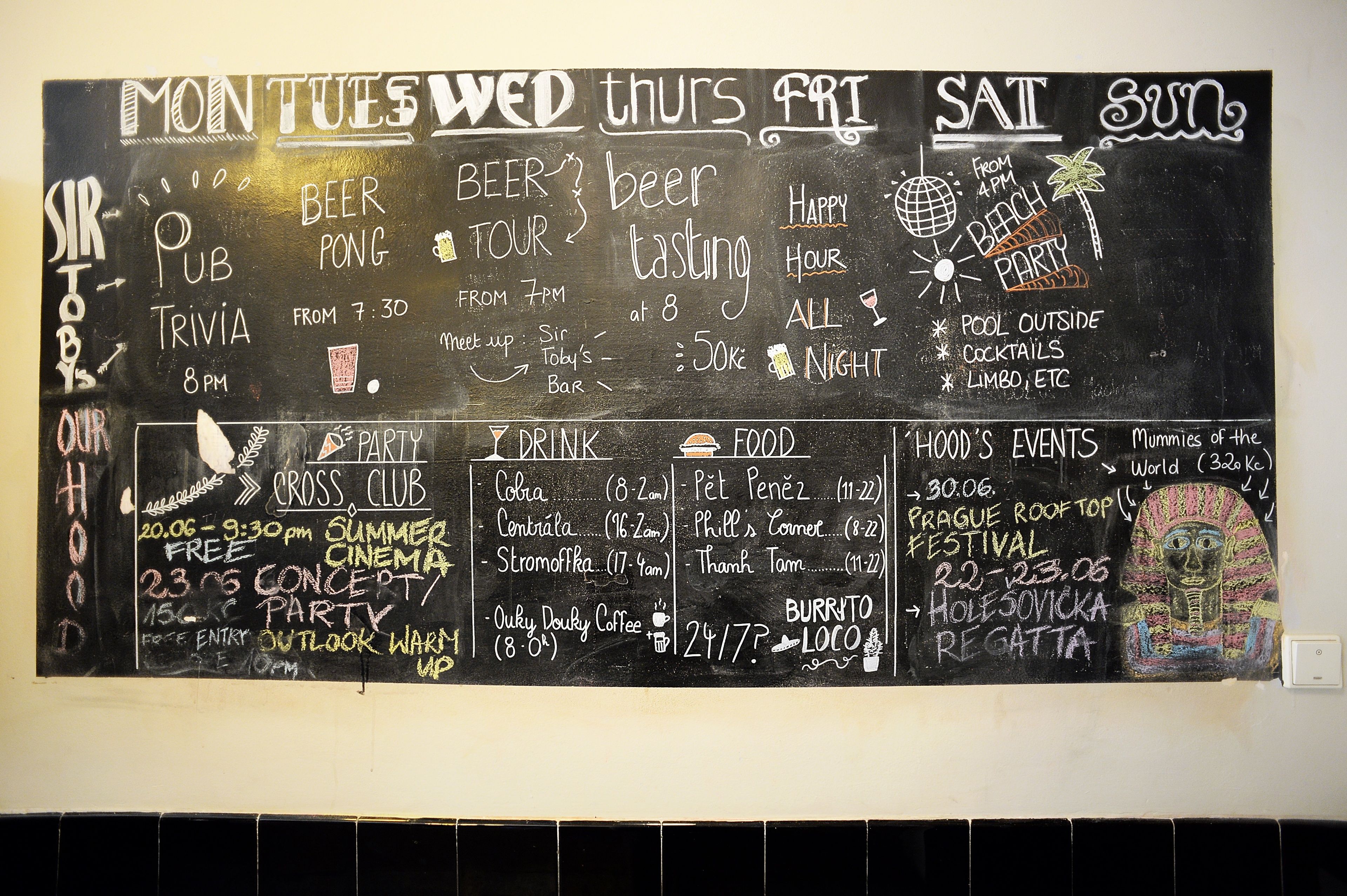Quadro negro com lista de eventos e horários para a semana, incluindo beer pong, quiz e tour de cerveja.