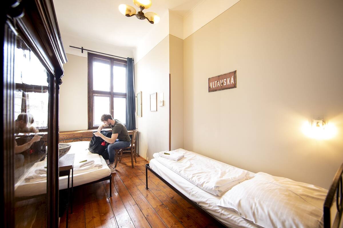 A small, cozy room with a single bed, a chair, a table, and a window with curtains.