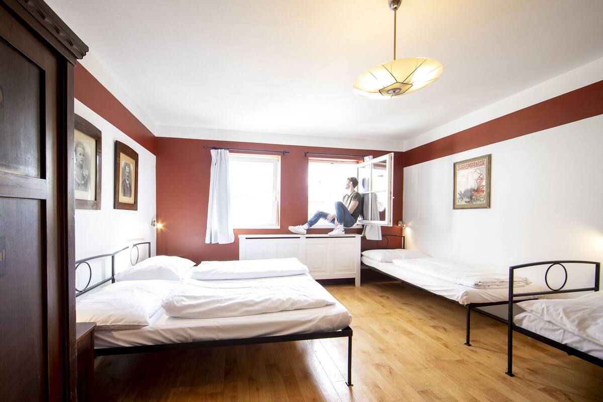 A room with two single beds, a desk, a chair, and a window with curtains.