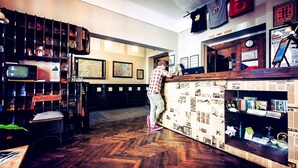 A bar area with a wooden counter, shelves with various items, and a television on the left. - Sir Toby's Hostel (Prague)