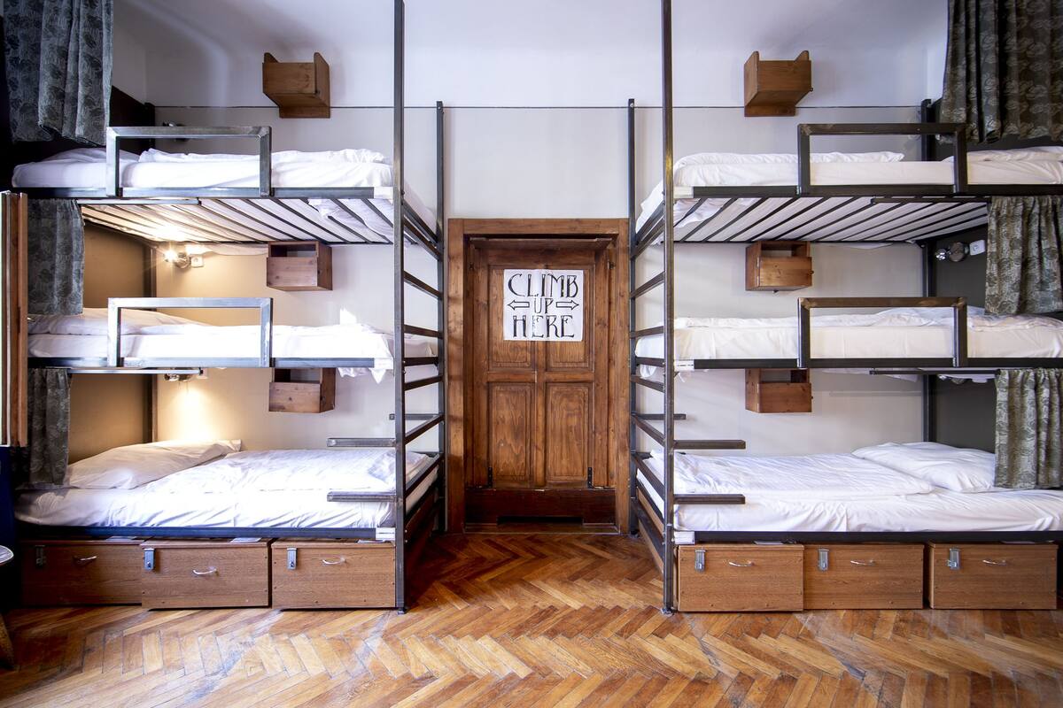 A dormitory room with bunk beds, wooden storage drawers, and a sign that says "CLIMB UP HERE".