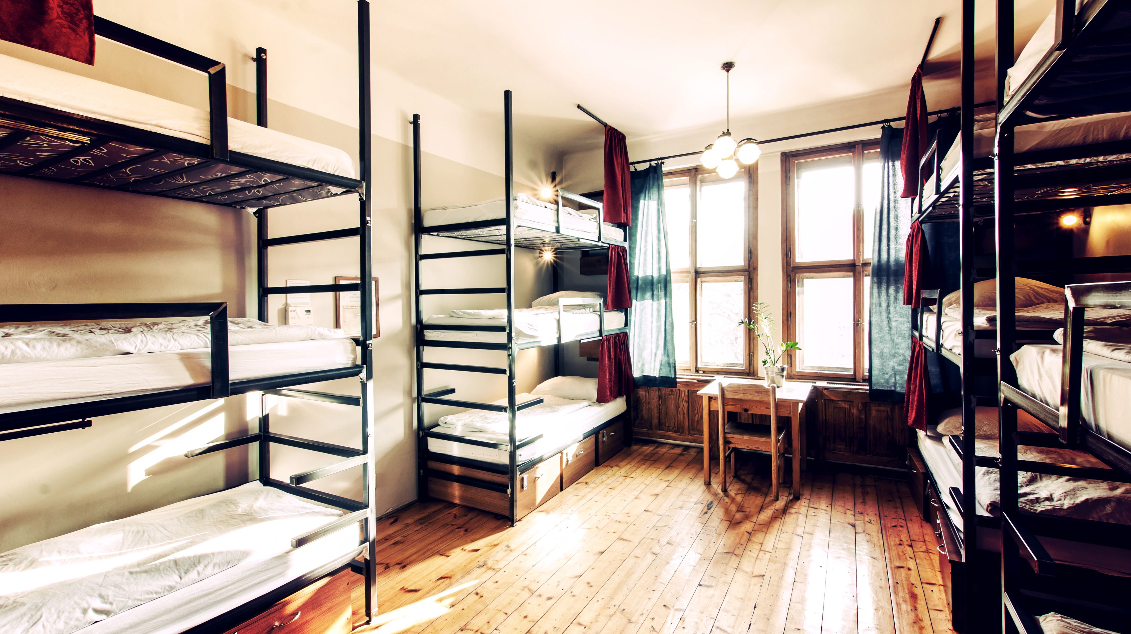 A dormitory room with bunk beds, a wooden desk, and a window with curtains.