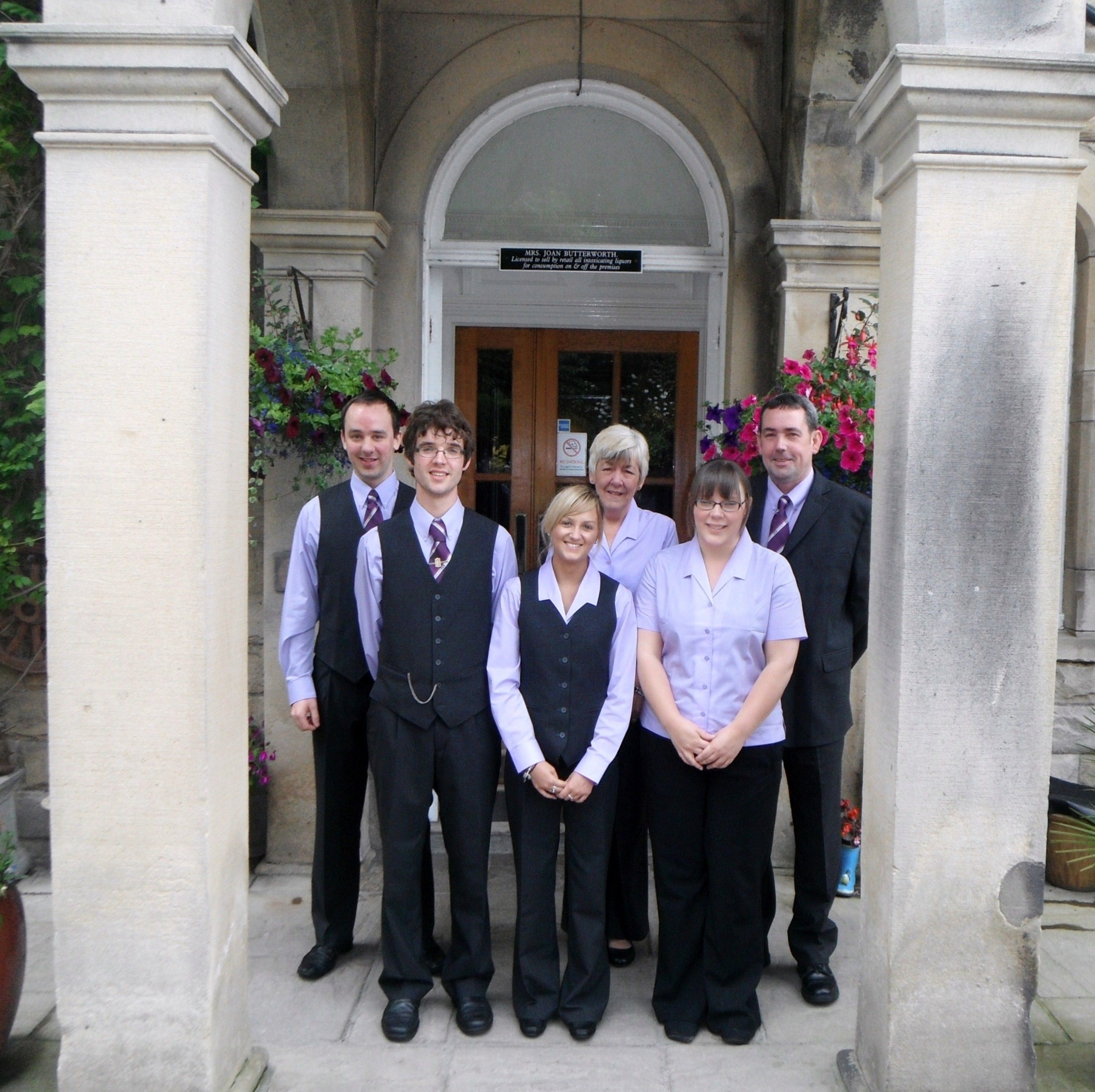 A group of people standing in front of a building with a sign that reads "MRS. JANE BUTTERWORTH".