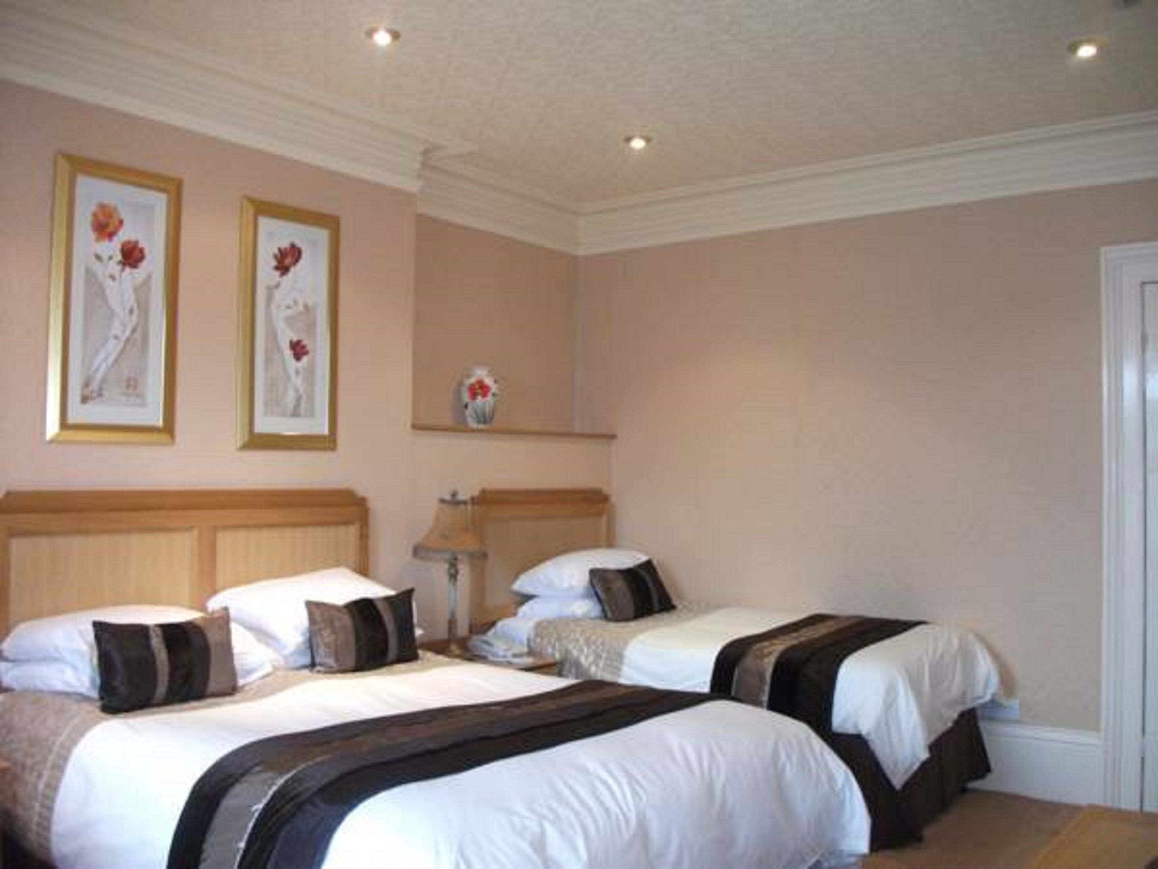 Habitación de hotel con dos camas, cada una con ropa blanca y cabeceros oscuros. En la pared, encima de las camas, hay cuadros con motivos florales.